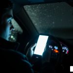 A driver glancing at a glowing phone screen in a dark car - how to prevent distracted driving