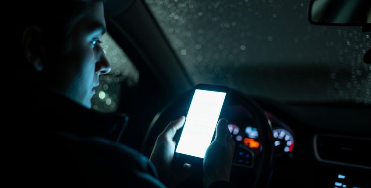 A driver glancing at a glowing phone screen in a dark car - how to prevent distracted driving